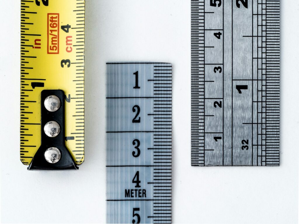 A yellow tape measure beside two metal rulers marked in inches and centimeters on a white table